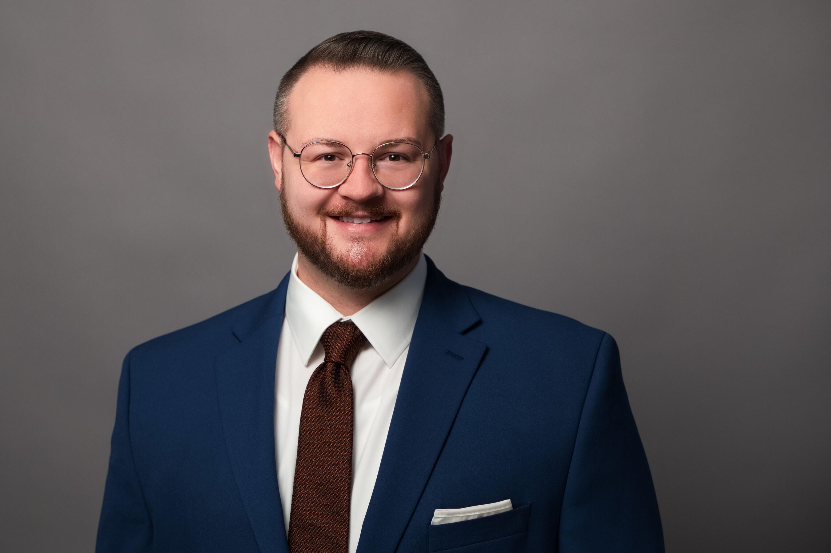 Chanan Brown Headshot Headshot of Chanan Brown, a white man wearing round silver glasses, a white dress shirt, a copper tie, and a dark blue suit jacket. The photo is cropped to a wide rectangle and shows Chanan from the chest up in front of a soft grey backdrop.