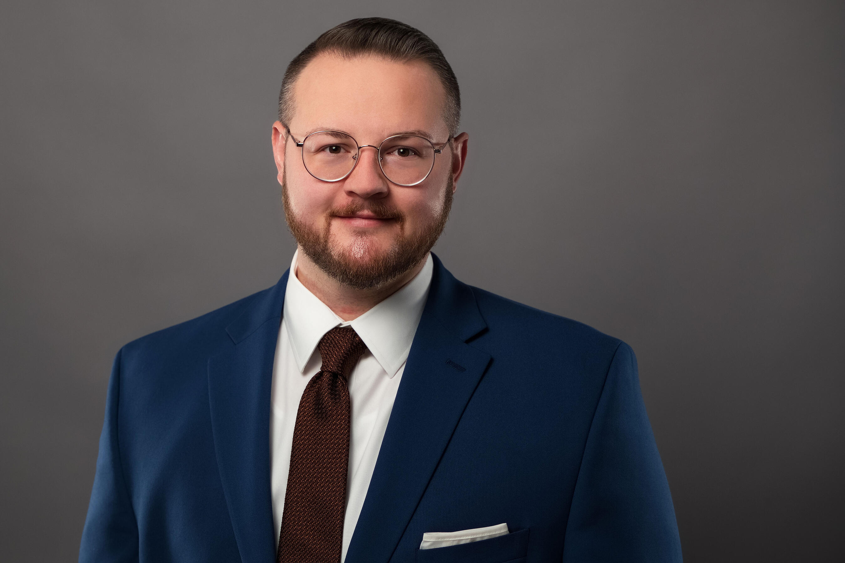 Chanan Brown Headshot Headshot of Chanan Brown, a white man wearing round silver glasses, a white dress shirt, a copper tie, and a dark blue suit jacket. The photo is cropped to a wide rectangle and shows Chanan from the chest up in front of a soft grey backdrop.
