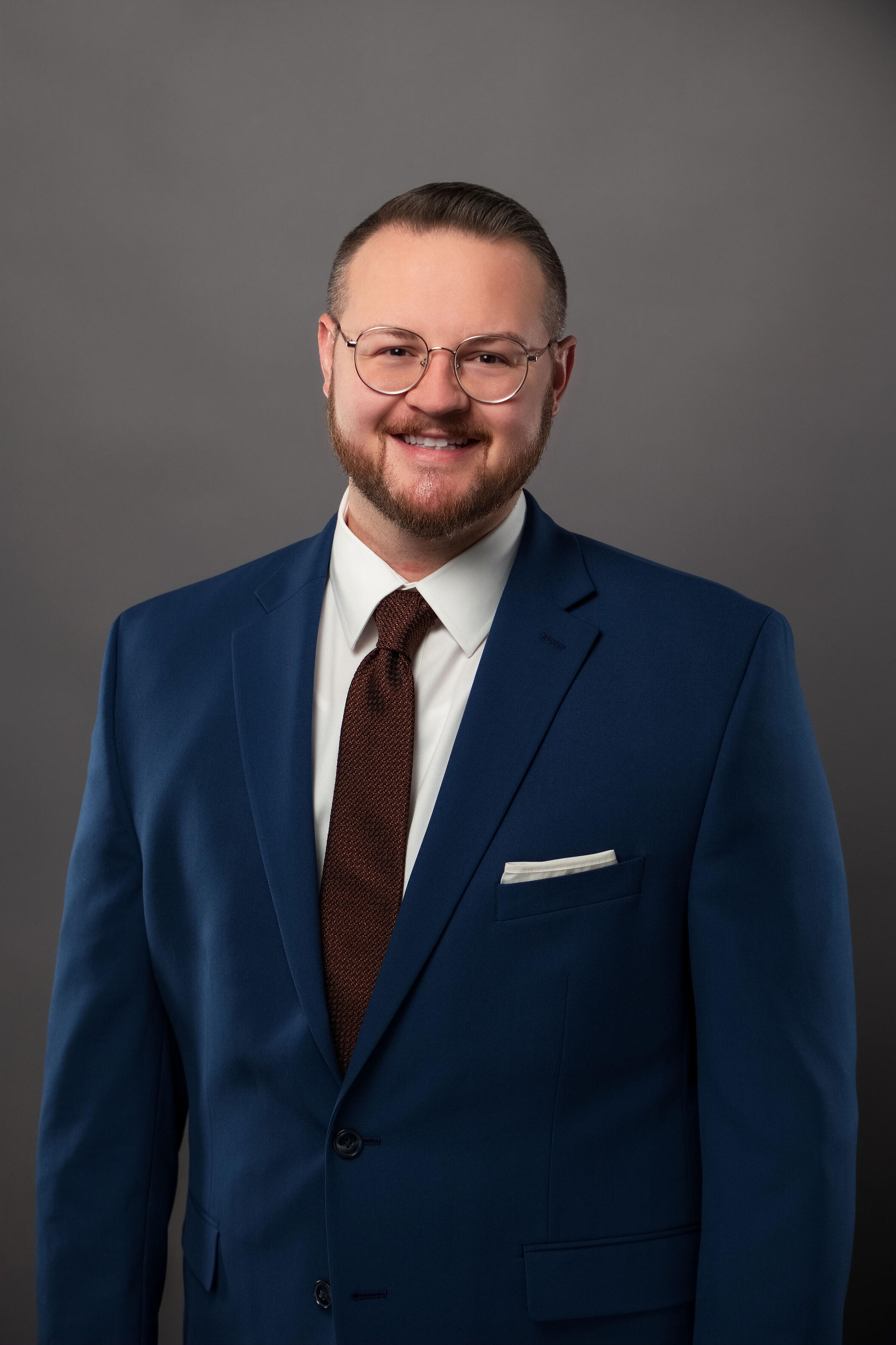 Chanan Brown Headshot Headshot of Chanan Brown, a white man wearing round silver glasses, a white dress shirt, a copper tie, and a dark blue suit jacket. The photo is cropped to a vertical rectangle and shows Chanan from the waist up in front of a soft grey backdrop.